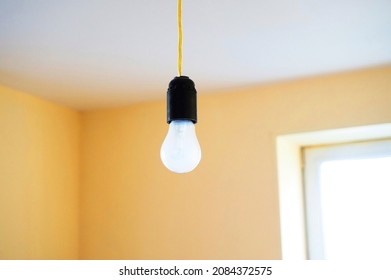 Light bulb hanging from ceiling on golden wire in orange pink room