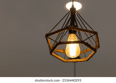 A light bulb hanging from a rope in a room. The light is on and the room is dimly lit - Powered by Shutterstock