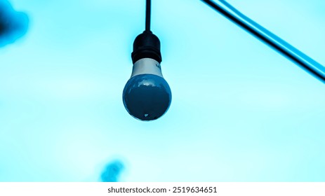 A light bulb hanging from a wire. The light bulb is blue and white. The sky is blue and clear - Powered by Shutterstock