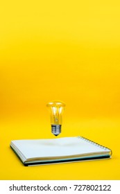Light bulb levitating above the notebook as a concept of new idea, copyspace, yellow background.