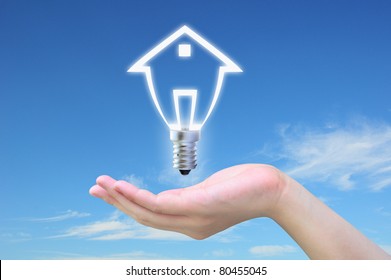 Light Bulb Model Of A House In Women Hand On Sky