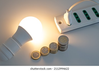 Light bulb on, with coins and a socket and plug next to it. Increase in electricity tariffs. 