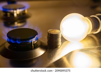 Light bulb on next to lit gas cooker, with coins next to it. Energy and gas costs, cost increases. - Shutterstock ID 2090095375