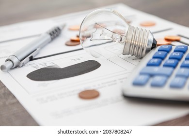 A light bulb, a pen, a calculator and some copper euro cent coins lie on top of an electricity bill. - Shutterstock ID 2037808247
