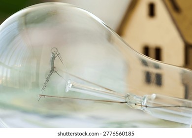 A light bulb is placed next to a small house model with its filament clearly visible during the day.