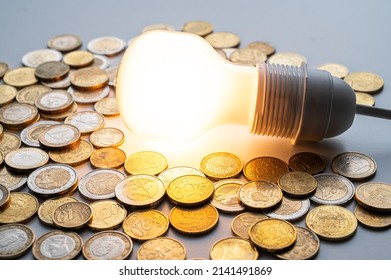 Light bulb turned on, with coins around. Increase in electricity tariffs, energy dependence, energy sources and energy supplies. 
 - Shutterstock ID 2141491869
