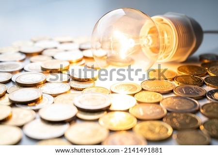 Light bulb turned on, with coins around. Increase in electricity tariffs, energy dependence, energy sources and energy supplies. 
 [[stock_photo]] © 