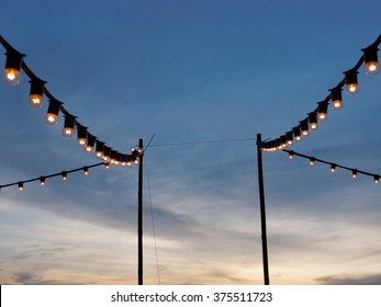 light bulbs on string wire hanging on poles against sunset sky - Powered by Shutterstock