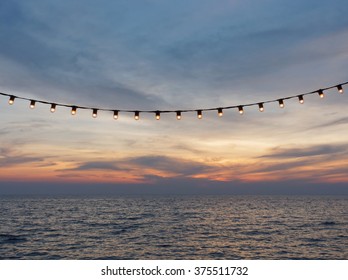 Light Bulbs On String Wire Against Sunset Sky By The Beach