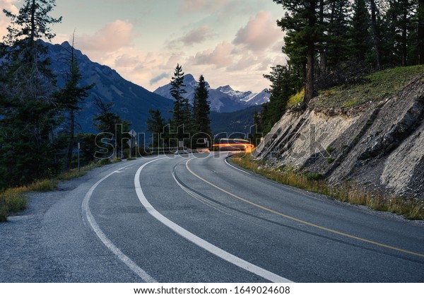 Light car on highway with rocky mountains in\
Banff national park at\
evening