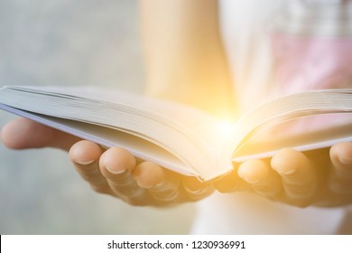 Light coming from book in woman's hands in gesture of giving, offering. Concept of wisdom, religion, reading, imagination.
