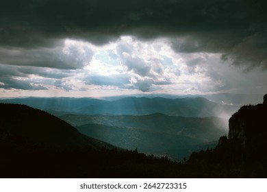 Light comming from storm clouds. White sun light surrounded by dark clouds an hills. 