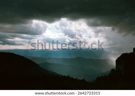 Light comming from storm clouds. White sun light surrounded by dark clouds an hills. 