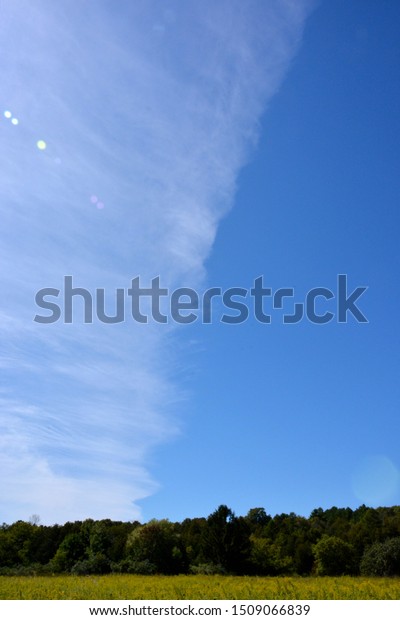 A\
light covering clouds creating a front with one side of the image\
with no clouds and the other with a thin layer of translucent\
clouds with green fields below in vertical\
view.\
