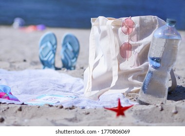 A Light Eco Bag Stands On A Caved Shore, At A Sledge, Near A Towel And Things. They Weigh Glasses On A Bag And A Bottle Of Water Is Standing Nearby. Resting-place