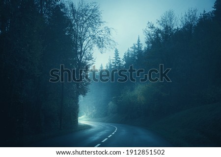 Light at the end of the empty road in the foggy forest