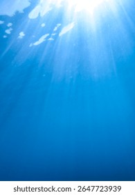 Light filtering down through blue water. Underwater sunlight in deep sea. Light viewed from blue abyss. Underwater sunlight shining deep under water with ripples on wave surface ocean ray, Background.