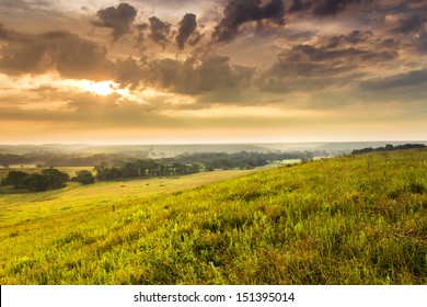 A light fog and heavy dew fills the valley as this sunrise warms the sky on a mild summer morning in the Kansas Tallgrass Prairie Preserve.