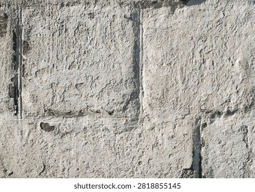 Light gray, almost white cinder block wall covered with lime chalk water-based paint. Old stone surface texture. Close-up.