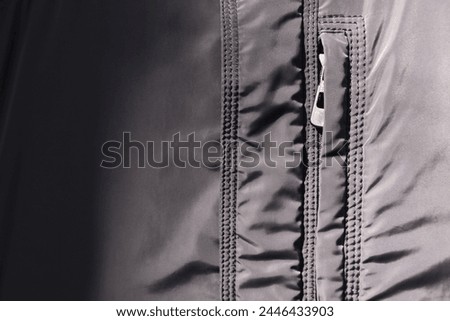 Light gray jacket close-up. Detailed fragment of a silver crepe jacket in a matte grayish color. Zipper, slider in clothing design with detailed display of seams and threads. View of fashion clothes