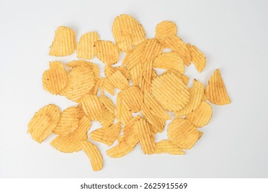 Light gray surface with scattered golden-yellow potato chips of varying sizes Indoor setting, artificial lighting