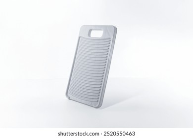 Light gray washboard, plastic material, upright on flat surface, white background, rectangular with rounded corners, vertical ridges, cut-out handle, manual clothes cleaning, functional simplicity