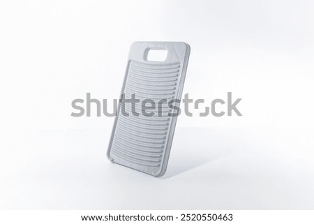 Light gray washboard, plastic material, upright on flat surface, white background, rectangular with rounded corners, vertical ridges, cut-out handle, manual clothes cleaning, functional simplicity