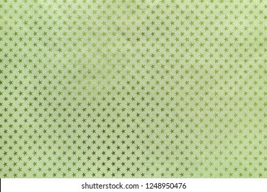 Light Green Background From Metal Foil Paper With A Pattern Of Sparkling Stars Closeup. Texture Of Olive Metallized Wrapping Holiday Paper Surface.