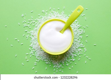 Light Green Bowl Of Rice Porridge For Babies On Green Background, Top View