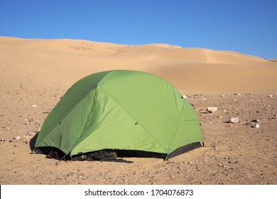 The light green tent and small stones around it in the desert near the big sandy hill, the blue sky.