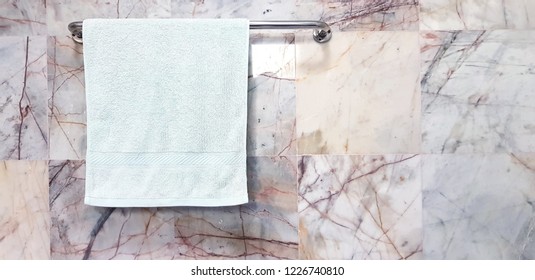 Light Green Towel Or Napkin Hang On Stainless Steel Hanger With White Marble Wall Background In Bathroom With Copy Space  - Cleaning, Shape And Surface Of Stone Concept 