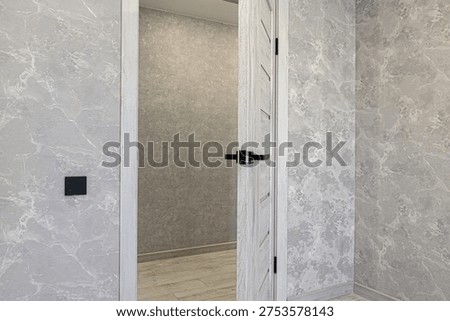 Light grey marble-patterned walls framing a white interroom door with black handle; light wood flooring, neutral textured wallpaper in adjacent room, sleek black switchplate