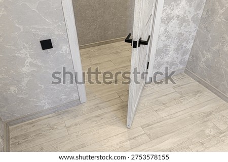 Light grey marble-patterned walls, white interroom door with black handles, light wood laminate flooring; minimalist design, neutral color scheme, sleek black switchplate.