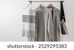 Light grey wool coat or jacket, merino sweater or dress, alpaca scarf and black leather bag on hanger against white wall background. Autumn and winter wool clothing. Trendy  monochrome fashion look.