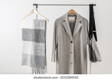 Light grey wool coat or jacket,  alpaca scarf and black leather bag on clothes hanger against white wall in home hallway. Autumn and winter wool  female clothing. Trendy monochrome fashion look. - Powered by Shutterstock