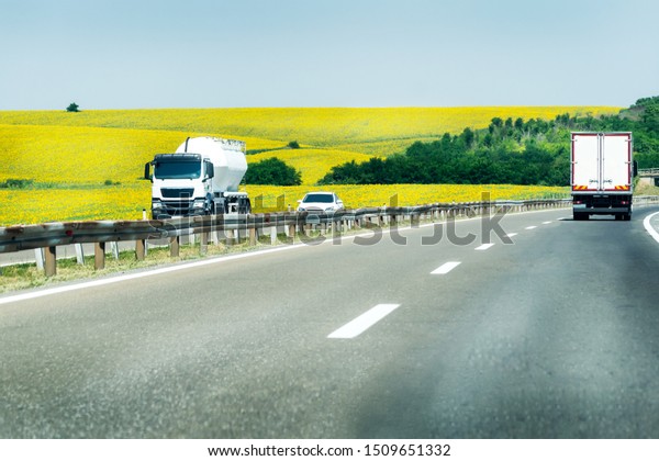 Light highway traffic on a beautiful\
summer day with fields of sunflowers in the\
background