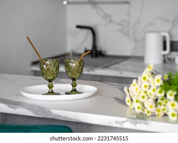 Light kitchen interior details. Two glasses with metal straws and flowers on marble bar counter at home. Stylish home interior. Minimalistic romantic table setting with drinks. Selective focus.