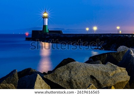The light of the lighthouse in Sassnitz is reflected on the water surface during the blue hour