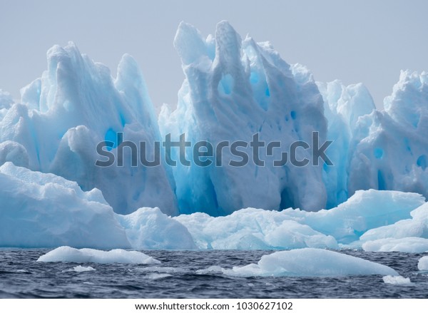 A light, medium and dark\
blue iceberg floating in the dark gray water of the Southern Ocean\
in Antarctic Sound. Overcast sky and a snow continent are in the\
background.