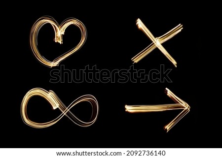 Light painting drawn heart, arrow, X letter and infinity sign, set of golden neon shapes against black background.