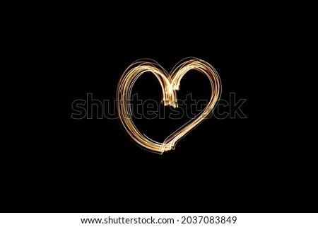 Light painting heart shape. Heart drawn with gold lights against black background. Long exposure photography. February 14 Valentine's Day background photo.
