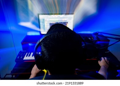 Light Painting Image Of Young Male Music Producer With Headphones, Working Sitting In Front Of Computer Screen In His Home Music Studio