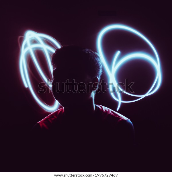 A light painting of a\
man in a dark room with light trails at the back. This picture is\
shot using a slow shutter speed and low iso to achieve the light\
trail effect.