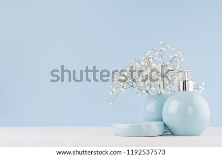 Light pastel blue ceramic acessories for bath  - bowl, vase, soap dispenser, flowers on white wood table. Decor for bathroom interior.