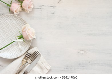 Light pastel colored tableware set: plate, vintage silverware on napkin and delicate pink roses on rustic shabby wooden background with copy space. Top view. - Powered by Shutterstock