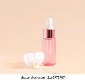 Light Pink Dropper Bottle near white orchid flower on light yellow, close up, mockup. Skincare beauty product, Aromatic oil or serum. Exotic cosmetics, pastel minimal composition