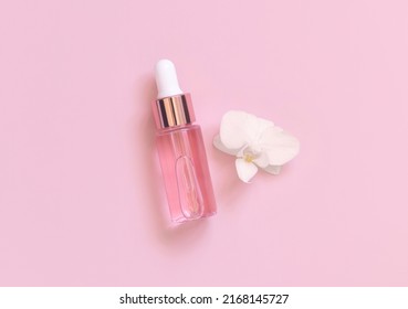 Light Pink Dropper Bottle near white orchid flower on light pink, top view, mockup. Skincare beauty product, Aromatic oil or serum. Exotic cosmetics, pastel minimal composition