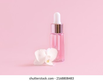 Light Pink Dropper Bottle near white orchid flower on light pink ,close up, mockup. Skincare beauty product, Aromatic oil or serum. Exotic cosmetics, pastel minimal composition