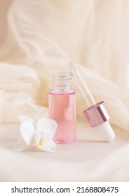 Light Pink opened Dropper Bottle near white orchid flower on light yellow, close up, mockup. Skincare beauty product, Aromatic oil or serum. Exotic cosmetics, pastel composition