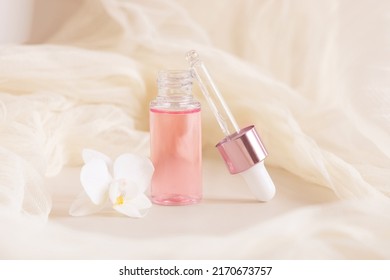 Light Pink opened Dropper Bottle near white orchid flower on light yellow, close up, mockup. Skincare beauty product, Aromatic oil or serum. Exotic cosmetics, pastel minimal composition